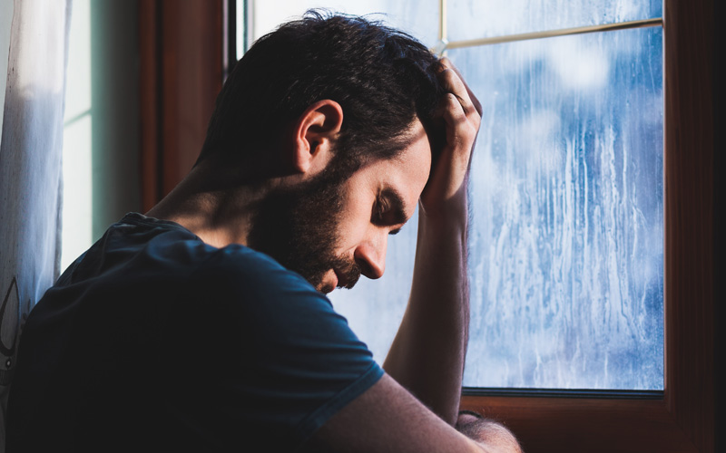 sad young man at the window while its raining