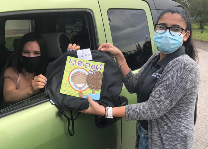 Champions for Children employee handing a mother a bag of supplies a book with a protective mask on
